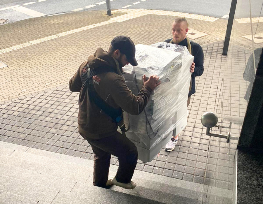 Reuter Umzüge: Das Umzugsunternehmen Köln trägt schwere, eingewickelte Maschine sicher eine Treppe hinauf.