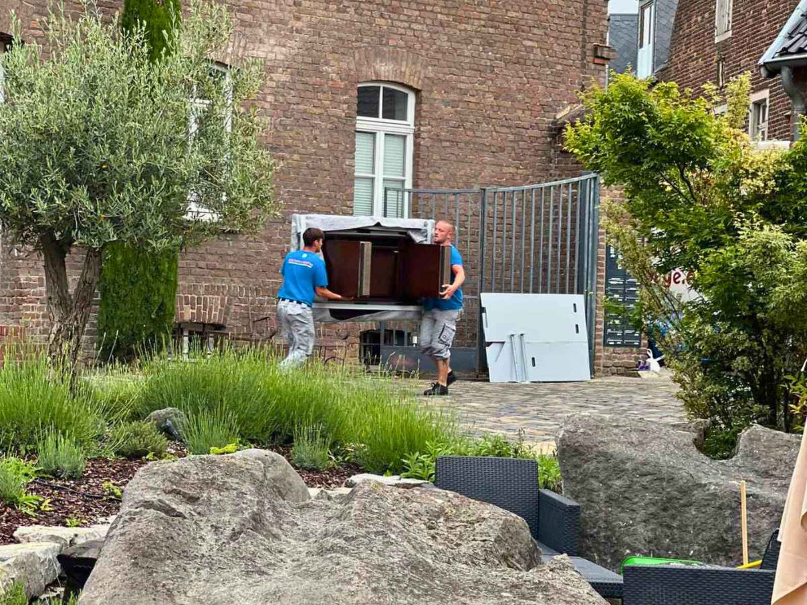 Reuter Umzüge – Umzugsunternehmen Köln beim sicheren Transport eines Möbelstücks aus einem Wohnhaus mit eingespieltem Team.